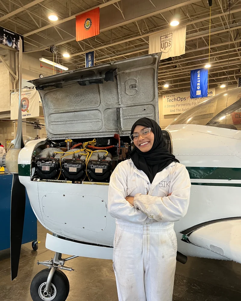 Zarin in a hangar beside a small aircraft with its engine cowling open