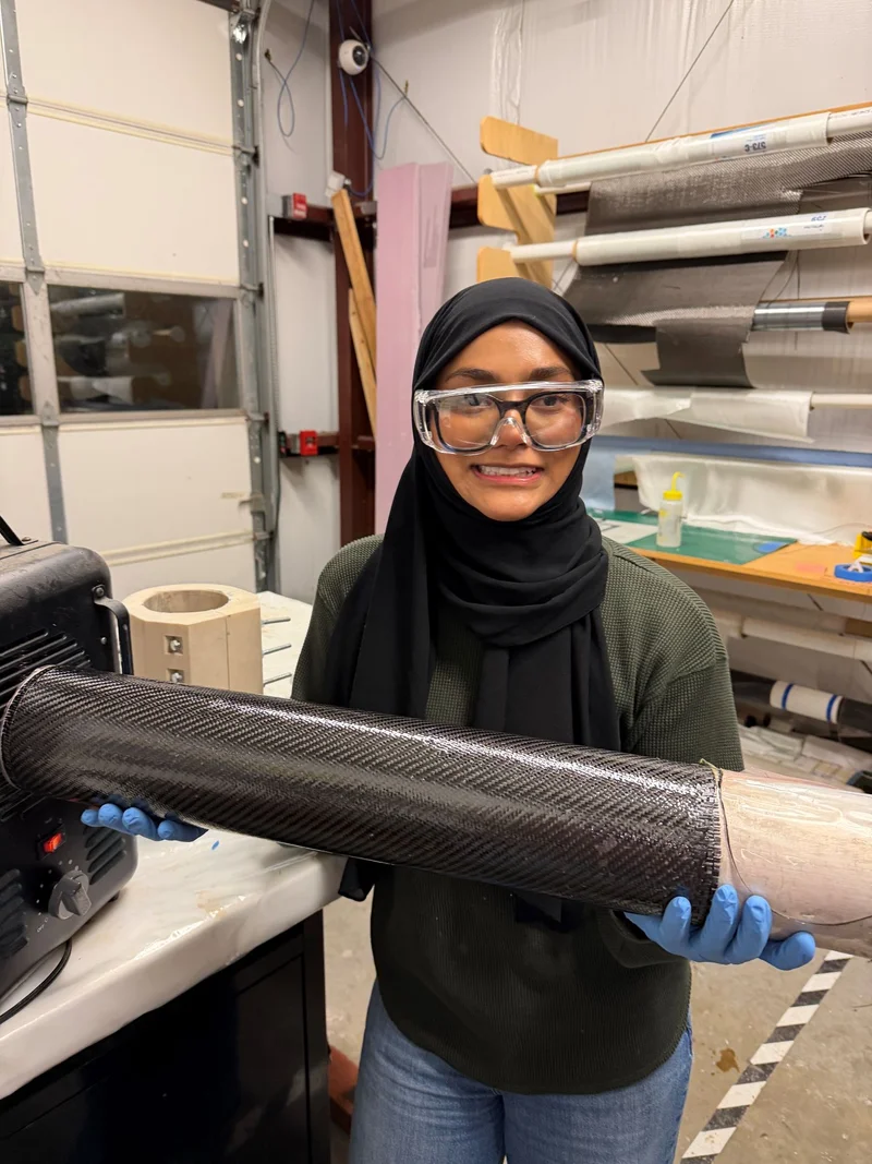 Zarin holding a carbon-fiber tube in a fabrication workshop