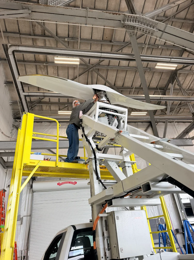 Zarin working beside a propeller assembly from an elevated platform in a hangar