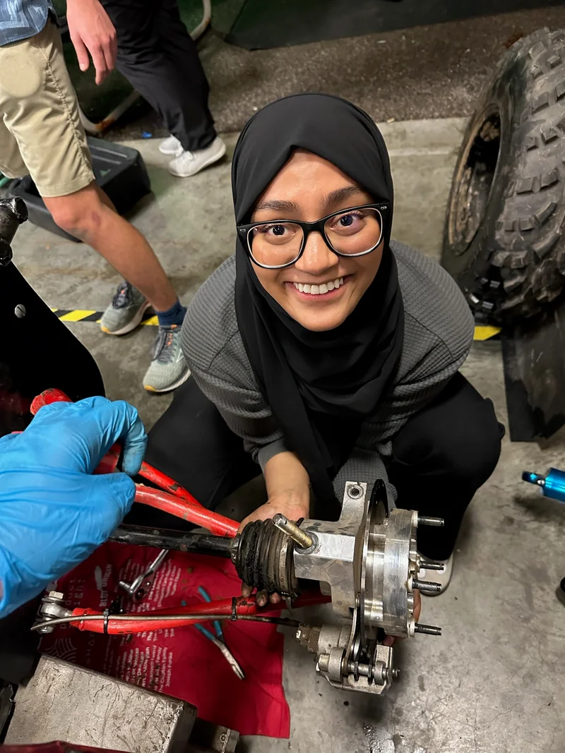 Zarin working beside a mechanical assembly on a workshop floor